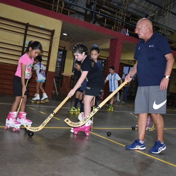 Grupo de niños practicando hockey sobre patines en un playón deportivo.
