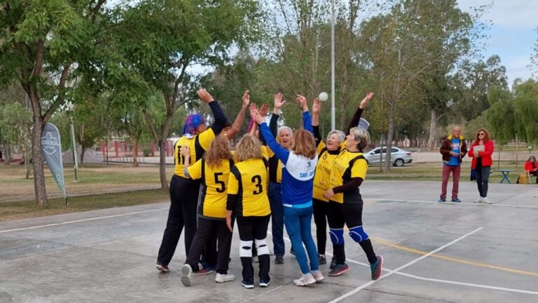 Grupo de adultos mayores participando en una clase de Newcom en un gimnasio municipal.